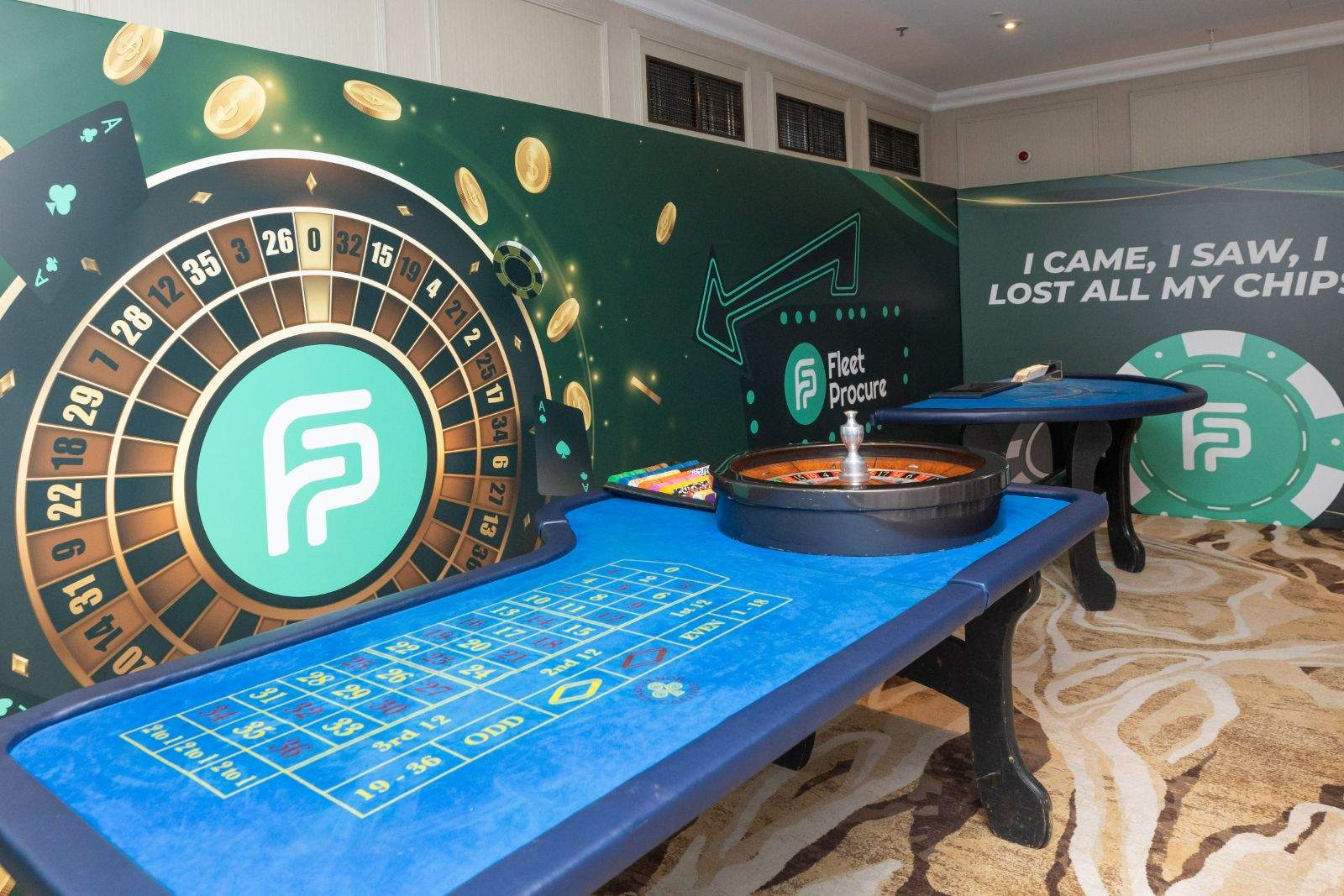 Casino-themed exhibition space for Fleet Procure, with a roulette table, a printed roulette-wheel backdrop and a wall reading I came, I saw, I lost all my chips