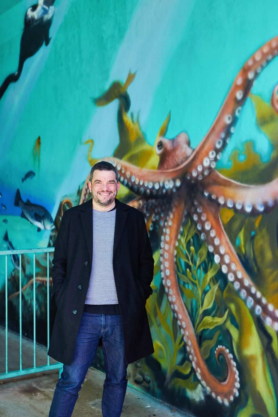 Tom smiling in front of a painted octopus mural